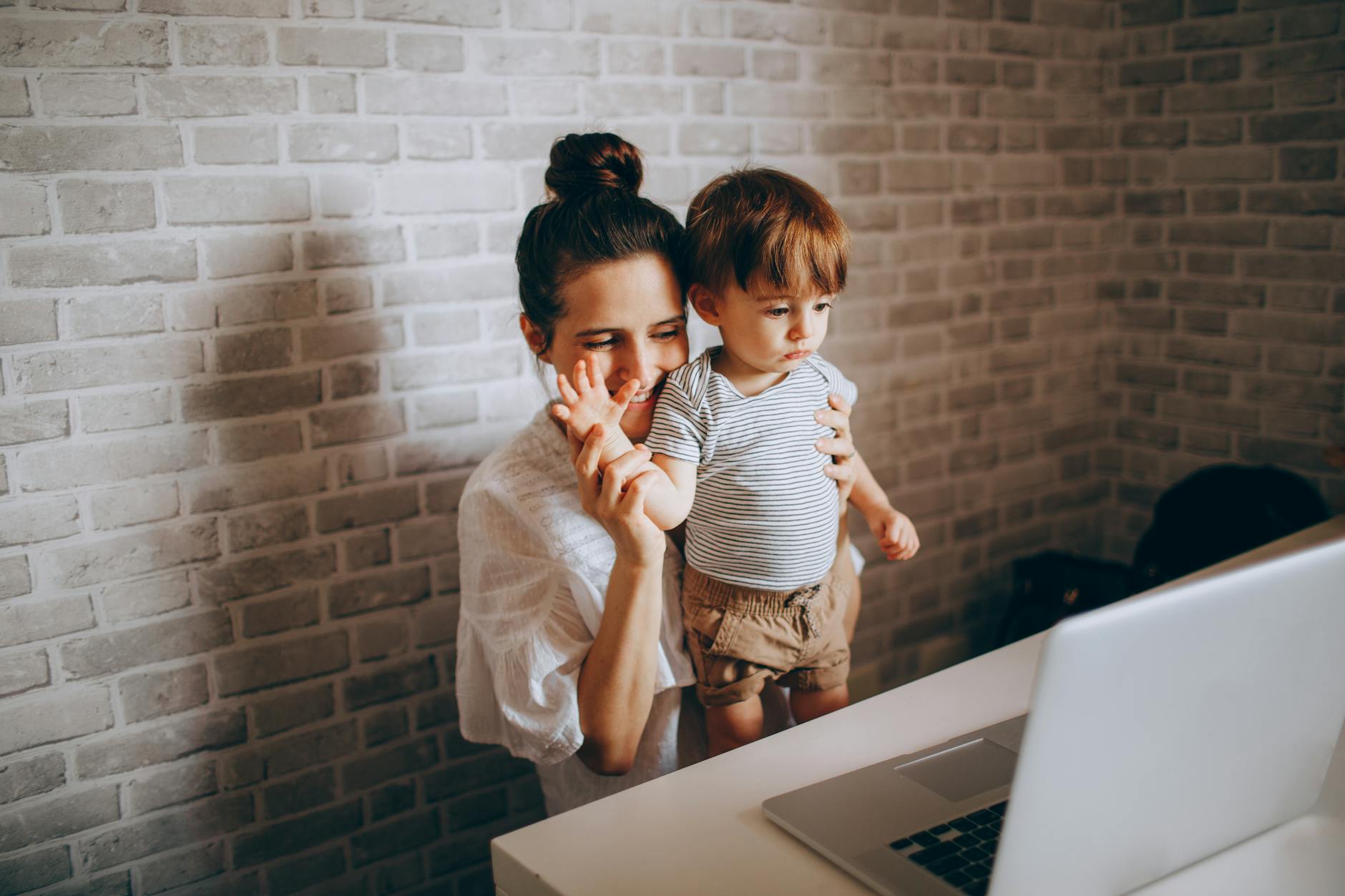 Mama z małym dzieckiem przy laptopie w przytulnym domowym wnętrzu