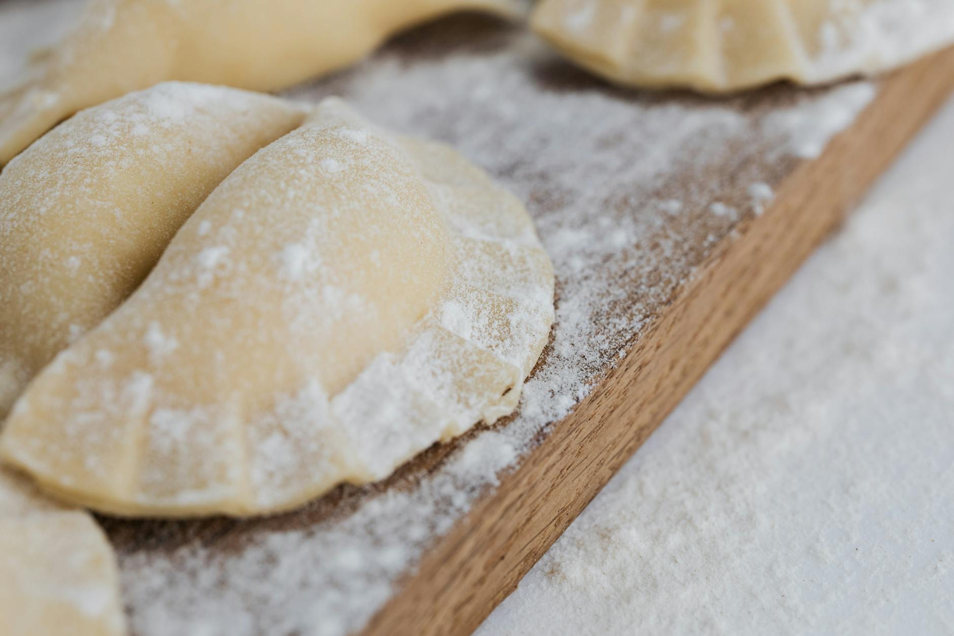 Świeżo zrobione pierogi posypane mąką na drewnianej desce