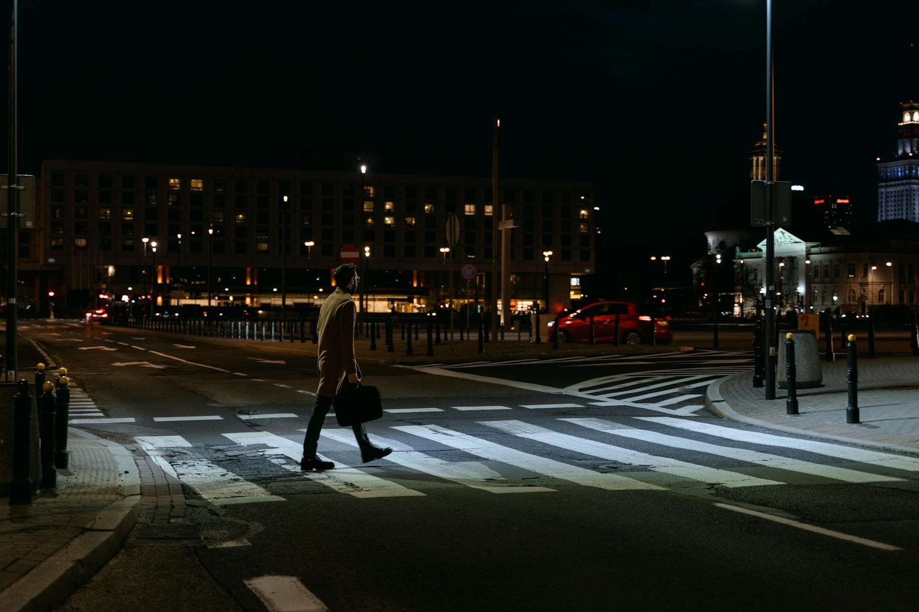 Mężczyzna z aktówką idzie nocą przez oświetloną miejską ulicę