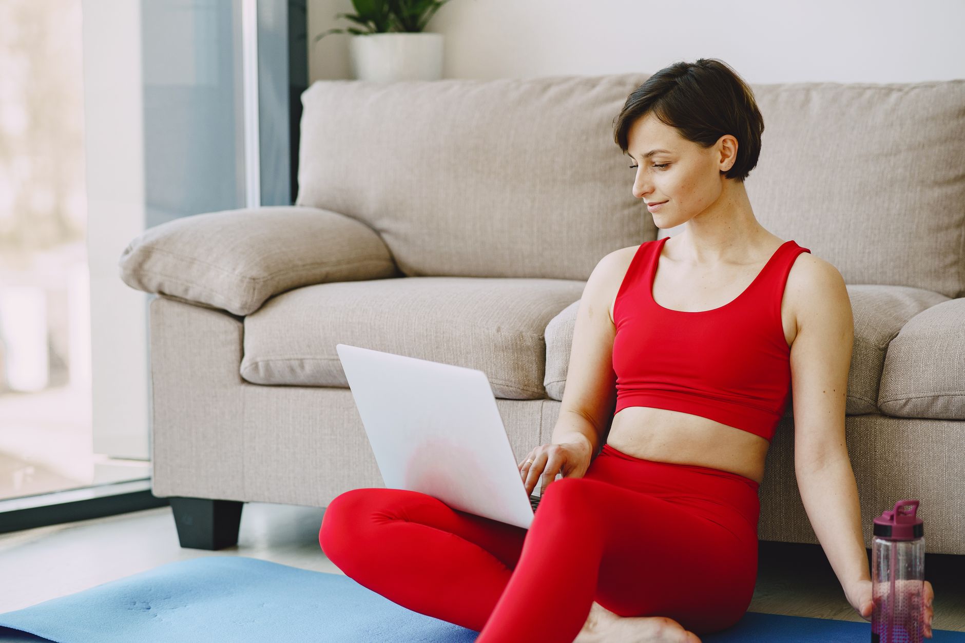Kobieta w sportowym stroju pracuje na laptopie na macie w salonie